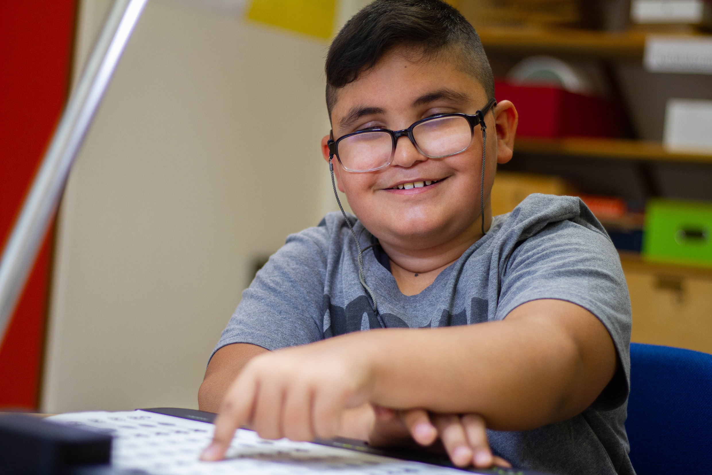 Hussein sits in front of the Tactonom Reader and tests a vocabulary graphic with funny sounds. He smiles happily.