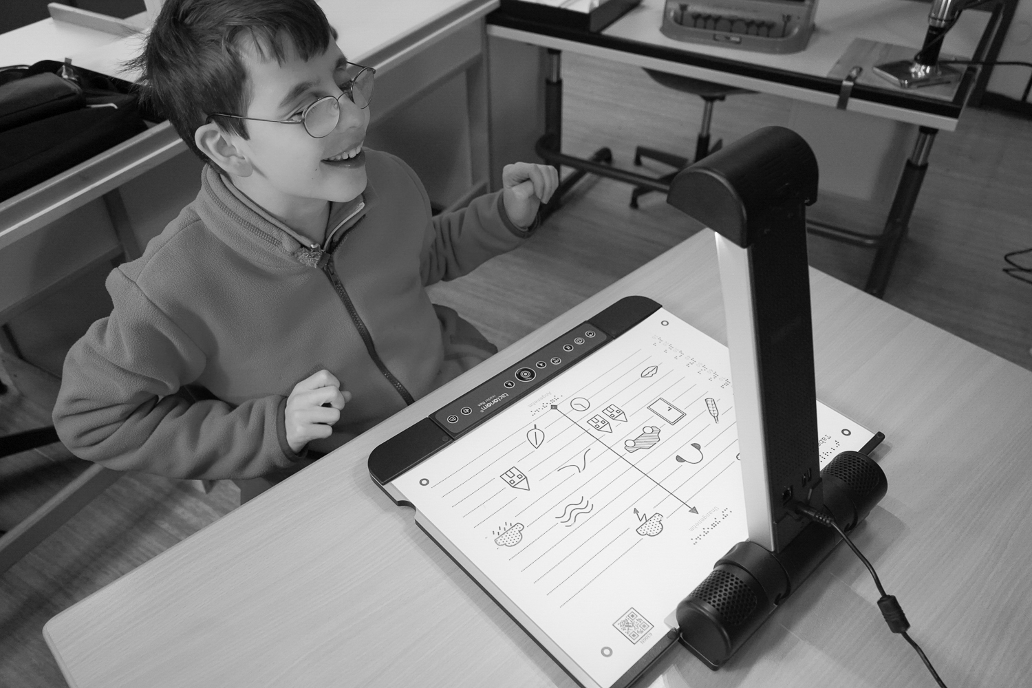 Ein BBS Nürnberg Schüler sitzt im Klassenzimmer vor dem Tactonom Reader Flex und freut sich an einer audio-taktilen Grafik, die gerade auf dem Tactonom Reader Flex aufliegt.